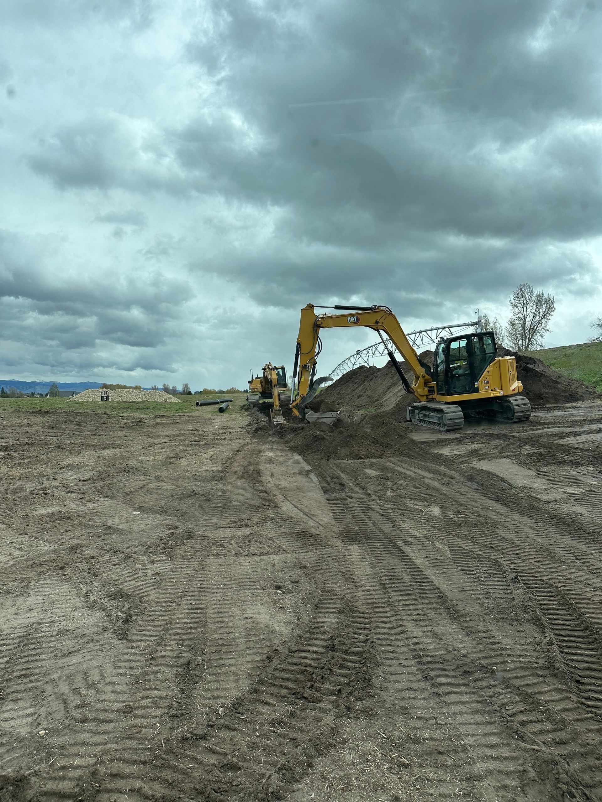 Yellow excavators working on a muddy construction site under cloudy skies