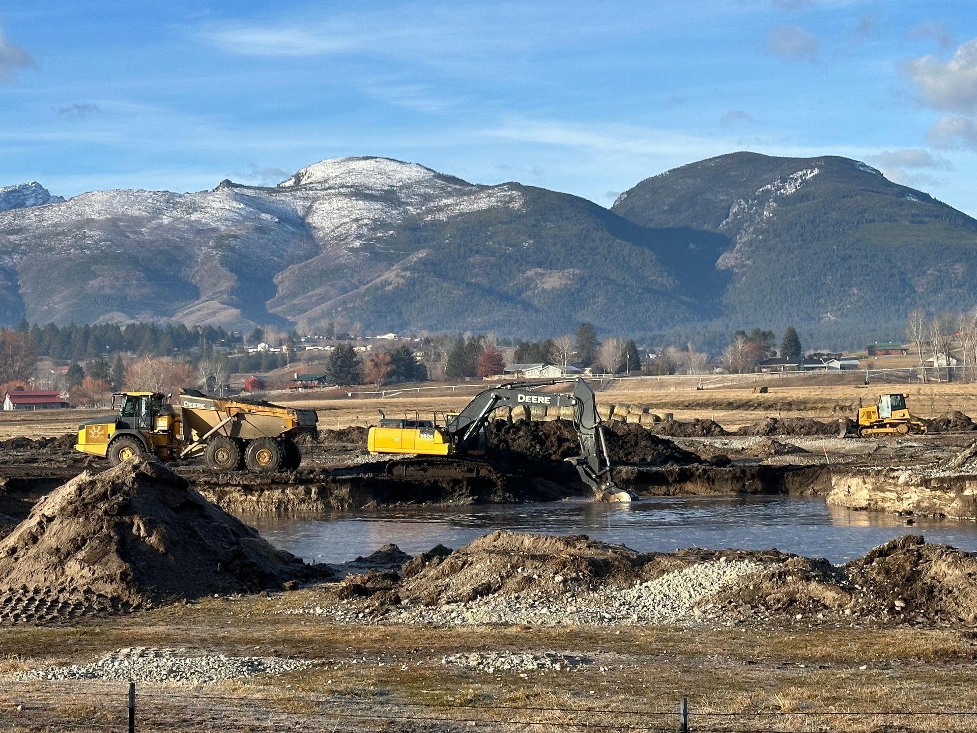 Construction site with heavy machinery, dirt mounds, and mountains under a blue sky