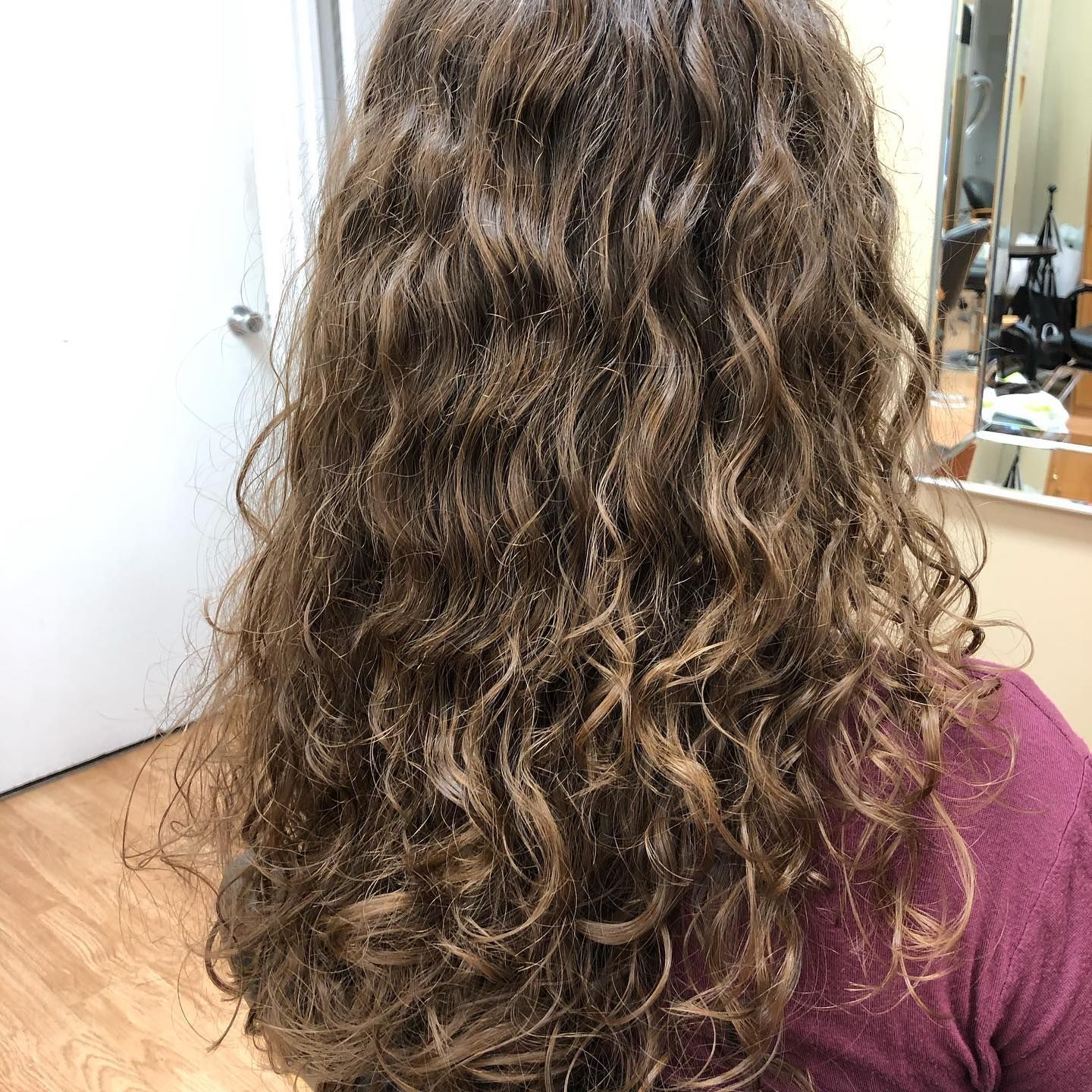 a woman with long curly hair is sitting in front of a mirror .