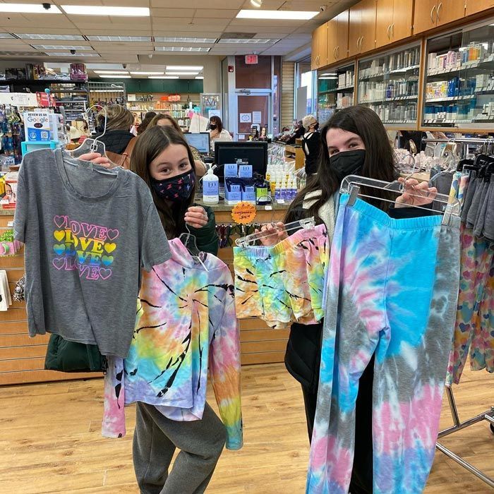 two women wearing face masks are holding tie dye shirts in a store .