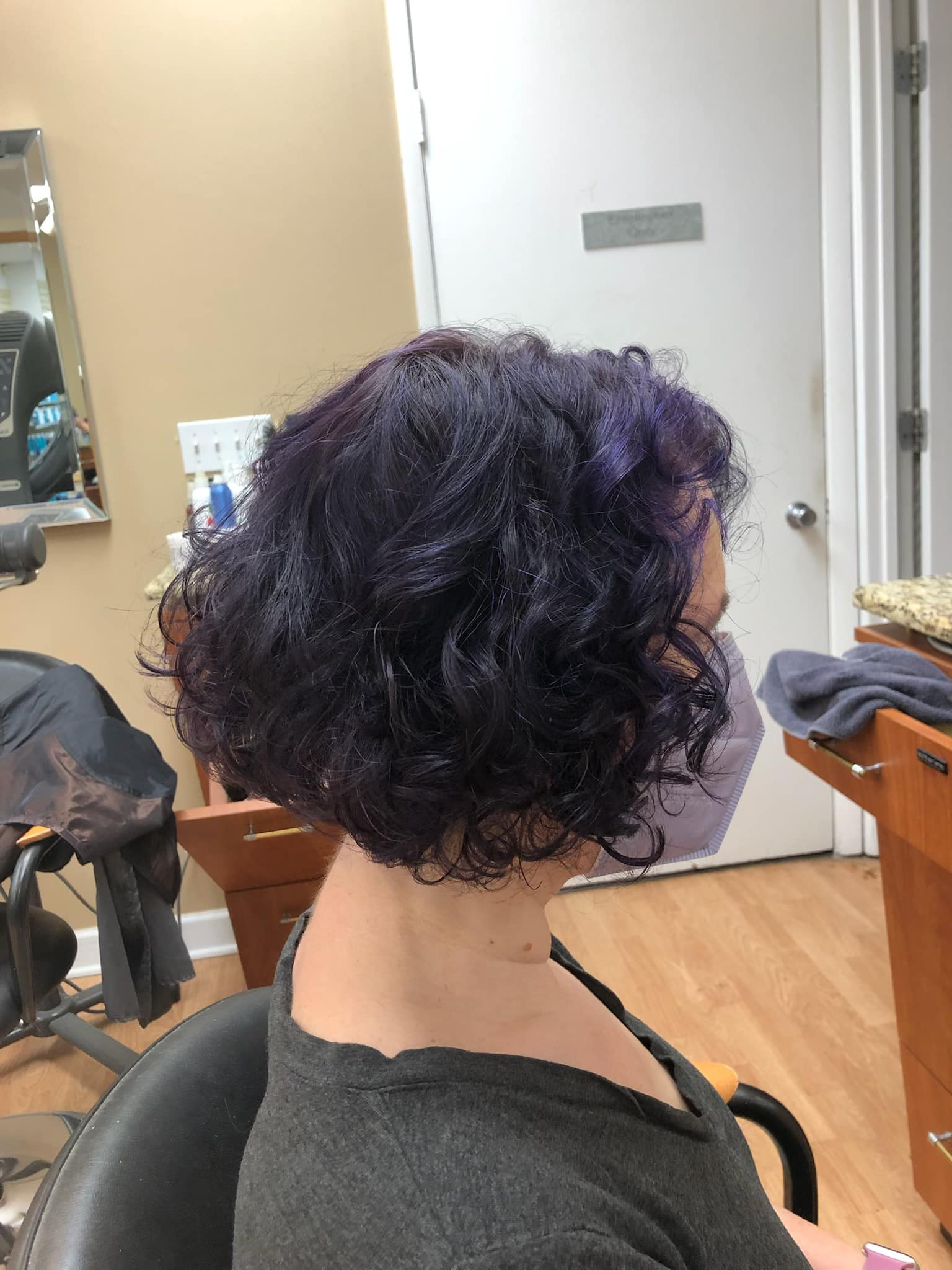 a woman with purple hair is sitting in a chair in a salon .