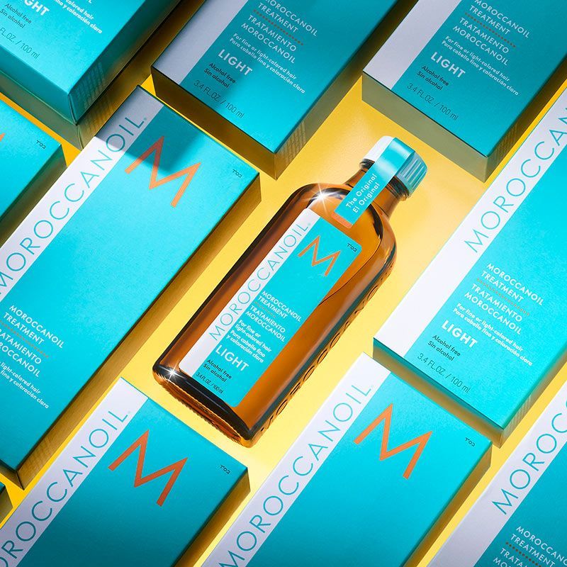 a bottle of moroccanoil light is surrounded by boxes on a yellow surface .