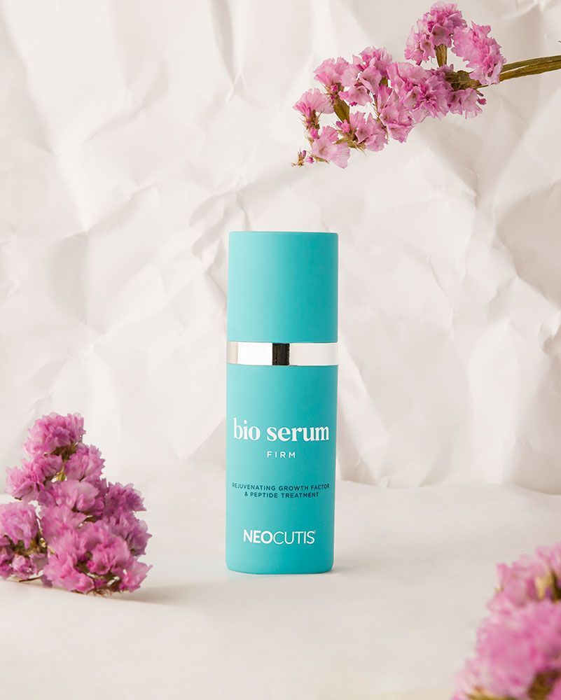 a bottle of bio serum is sitting on a table next to pink flowers .