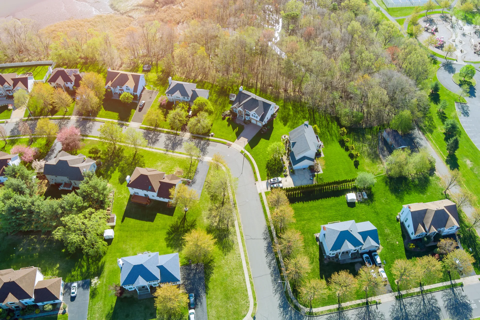 Aerial view of suburban houses with green lawns and a winding road.