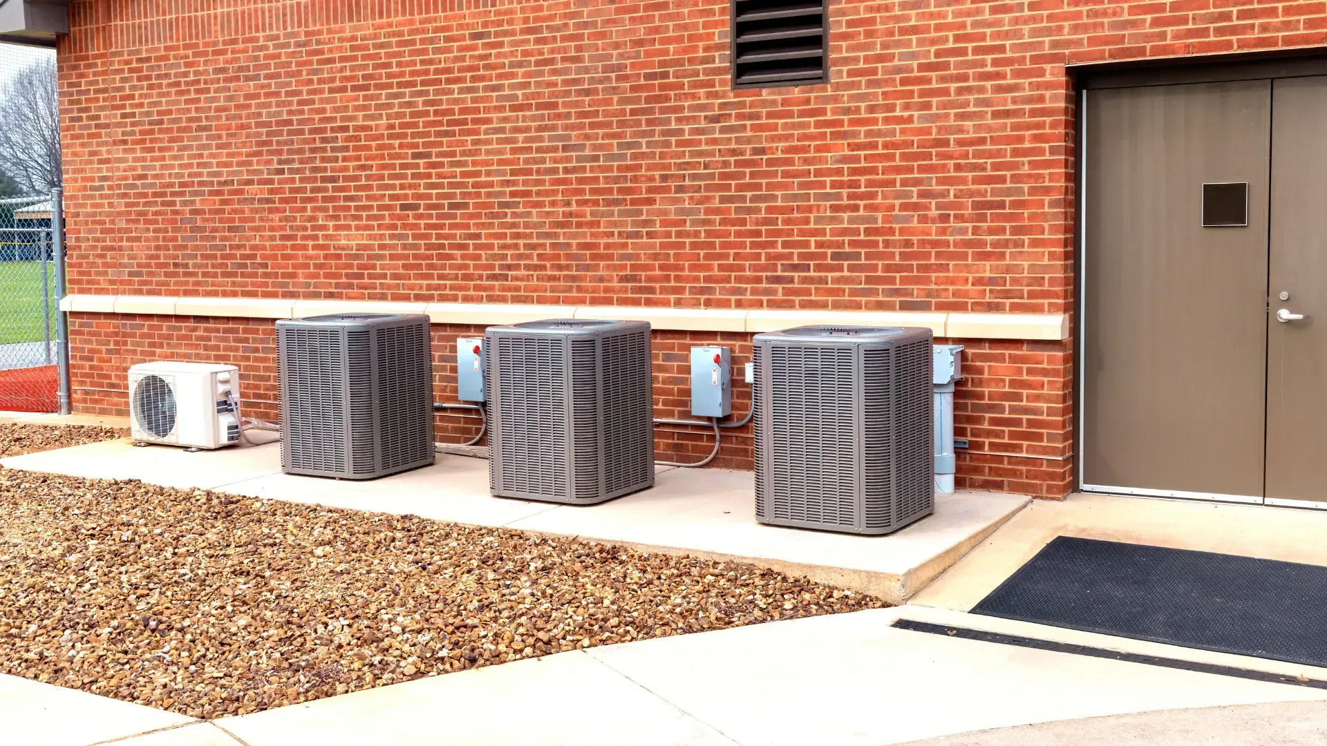 Three air conditioners are sitting outside of a brick building.