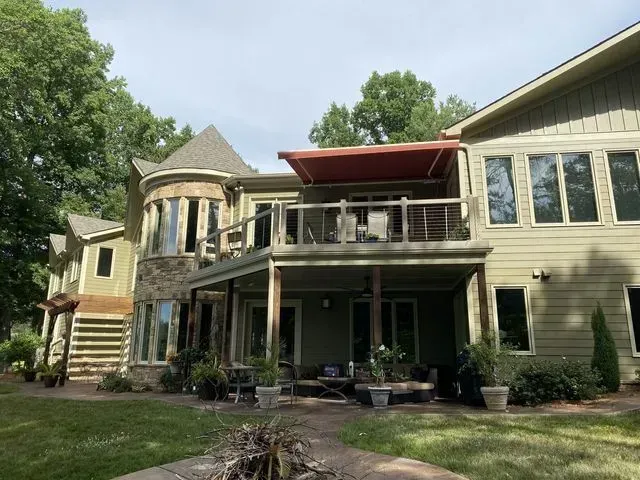 Two-story house with stone and beige siding, a deck, and a backyard patio surrounded by trees.