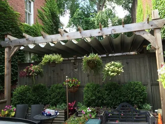 Backyard patio with wooden pergola, hanging flowers, and potted plants along a fence