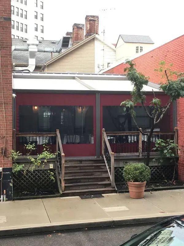 Front porch entrance with red awning, steps, and potted plants on a city street