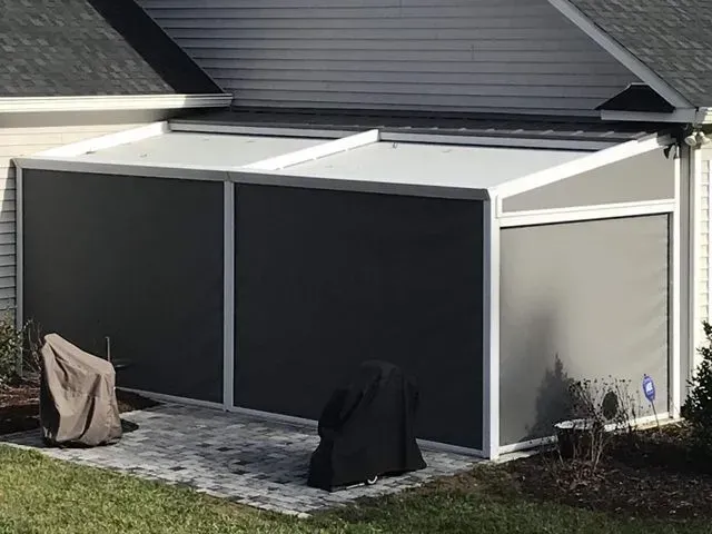 Covered patio with two large covered grill or storage units beside a house, in neutral gray and black tones