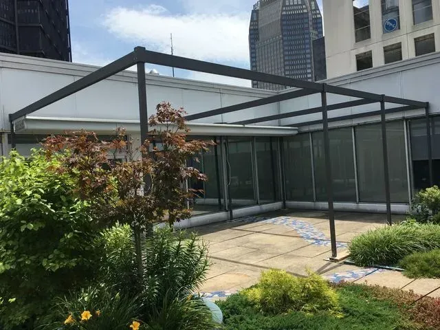 Modern rooftop garden with glass pavilion, patio path, and city skyscrapers in the background