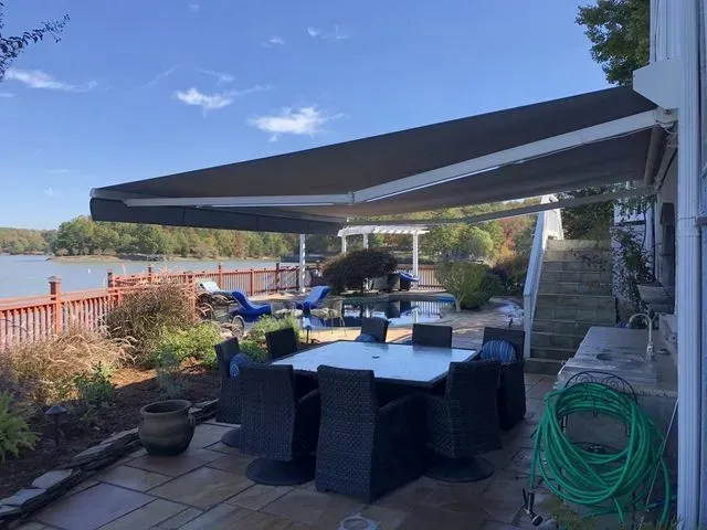 Patio dining area with a large awning, wicker chairs, table, grill, and garden view