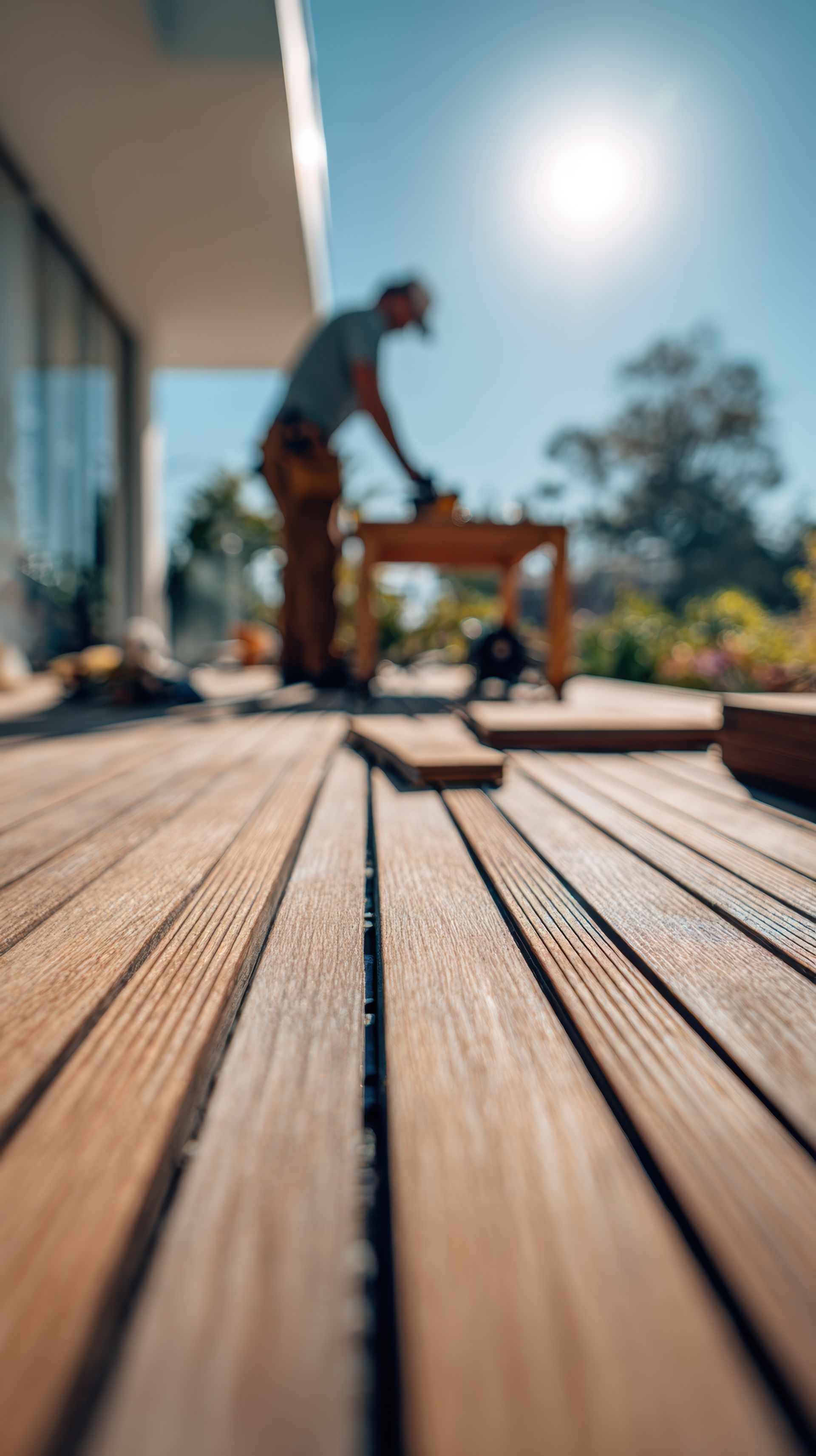 Outdoor wooden deck construction in progress with worker focused on carpentry tasks on a sunny day creating a natural backyard living space.