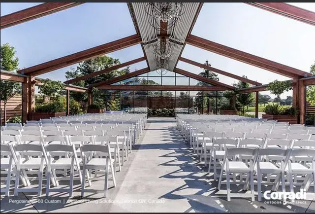 Outdoor wedding ceremony setup with rows of white chairs under a wooden pavilion and skylights