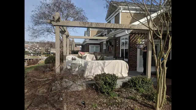 Covered outdoor patio with a pergola, patio furniture, and leafless trees beside a house.