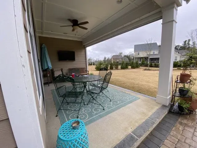 Covered patio with teal furniture, rug, and planter overlooking a grassy yard and neighboring homes.