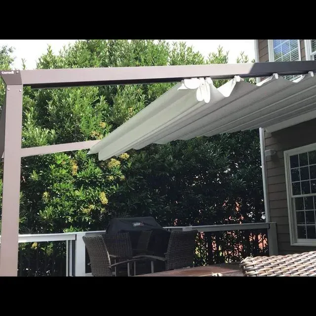 Patio with white retractable awning over outdoor table and chairs beside a house, backed by trees