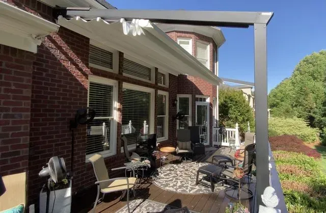 Brick patio with outdoor chairs and dining table beside a house under a white pergola on a sunny day