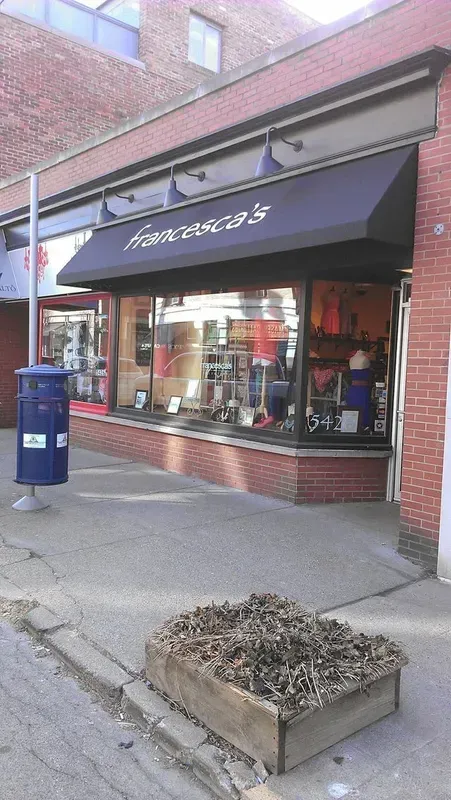 Brick storefront with dark awning and display windows beside a sidewalk and blue post box