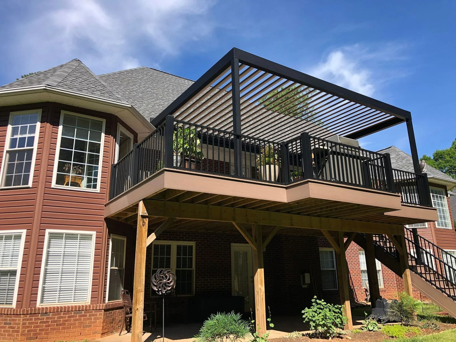 Brick house with elevated deck, black pergola, and stairs under a blue sky