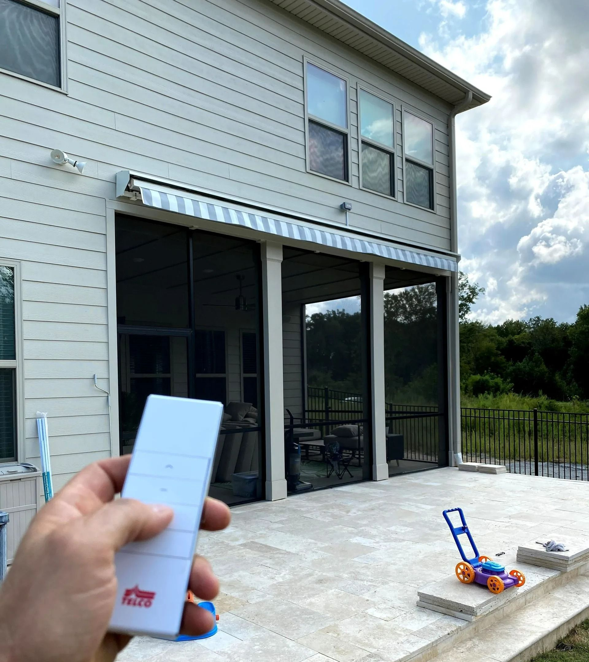 Hand holding a white remote control facing a house patio with sliding glass doors and a blue-and-red toy on the ground.