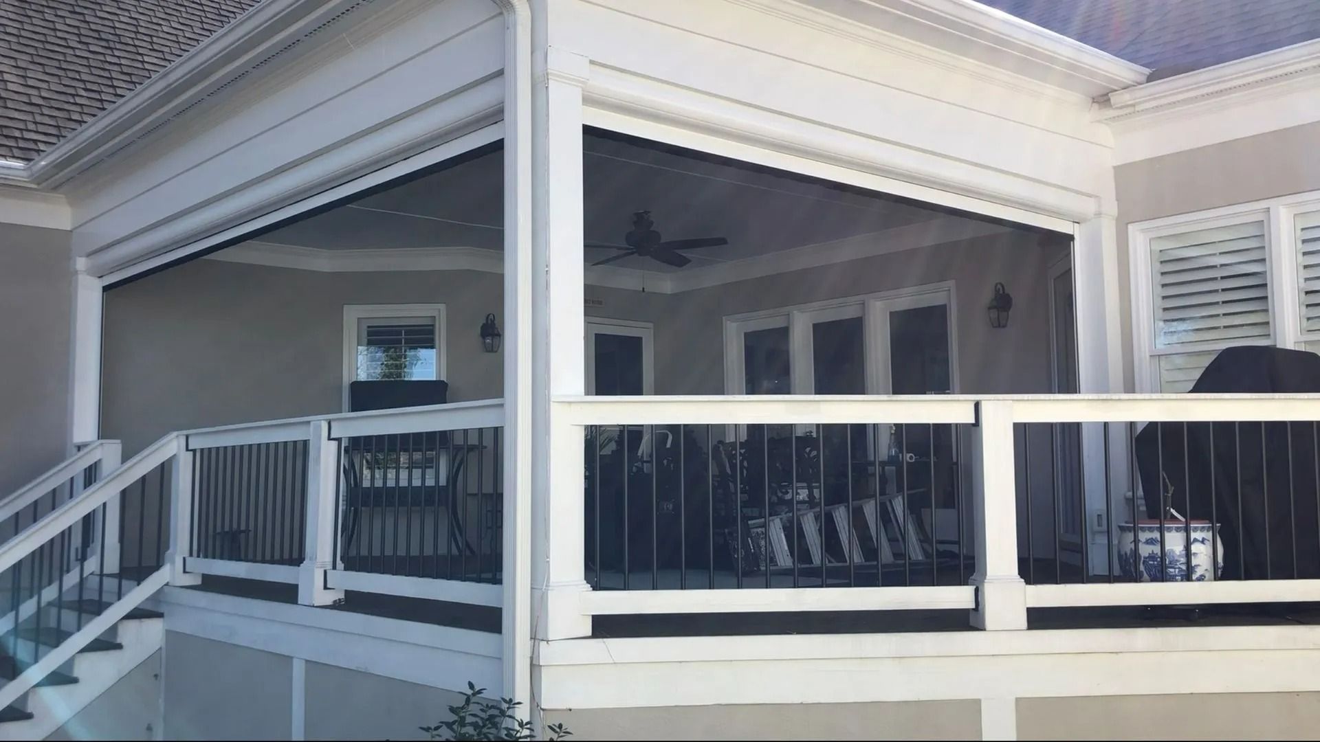 Covered porch with white railings and black chairs outside a house.