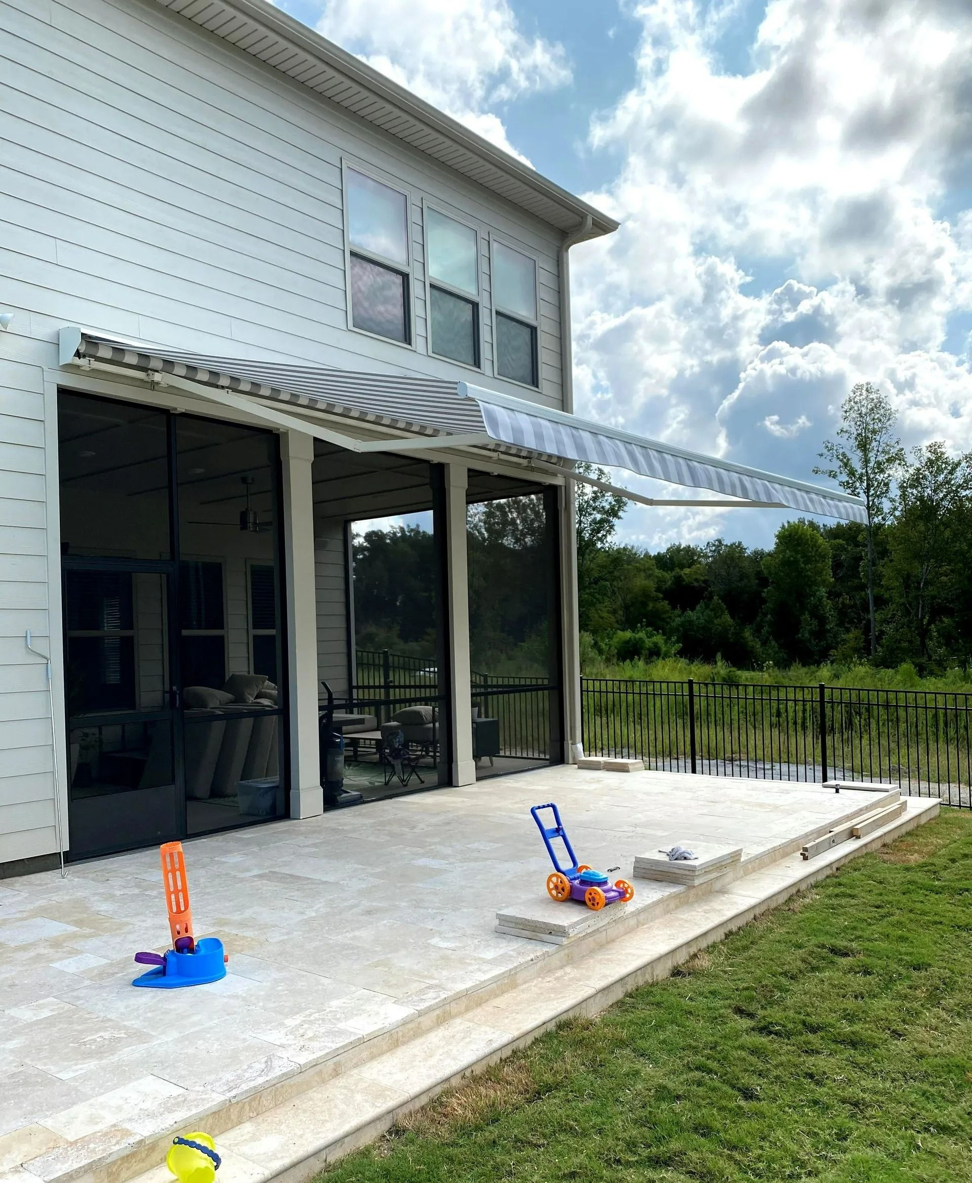 Patio with striped awning beside a modern house, with a slide and toys on the stone terrace.