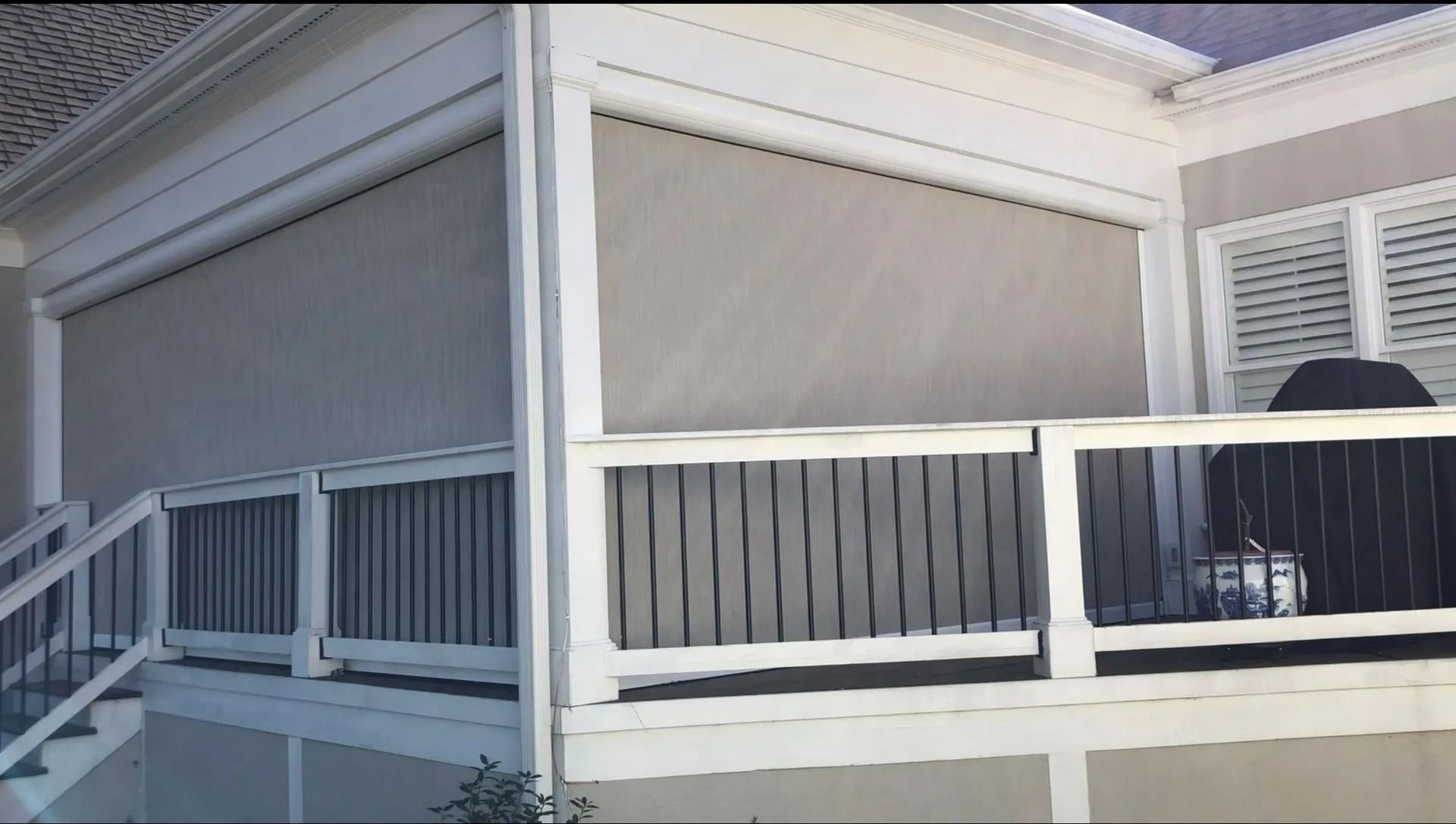 White screened porch with railings and a black grill near closed shutters