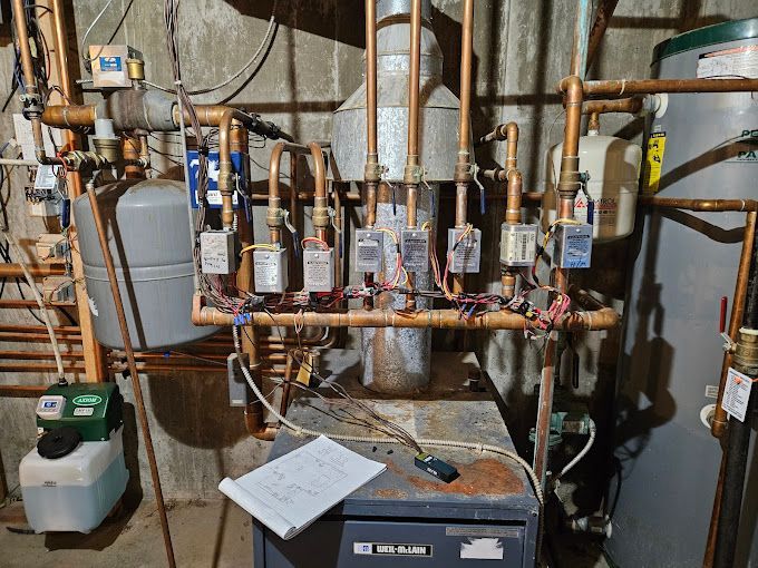 A boiler is sitting in a basement next to a water heater.