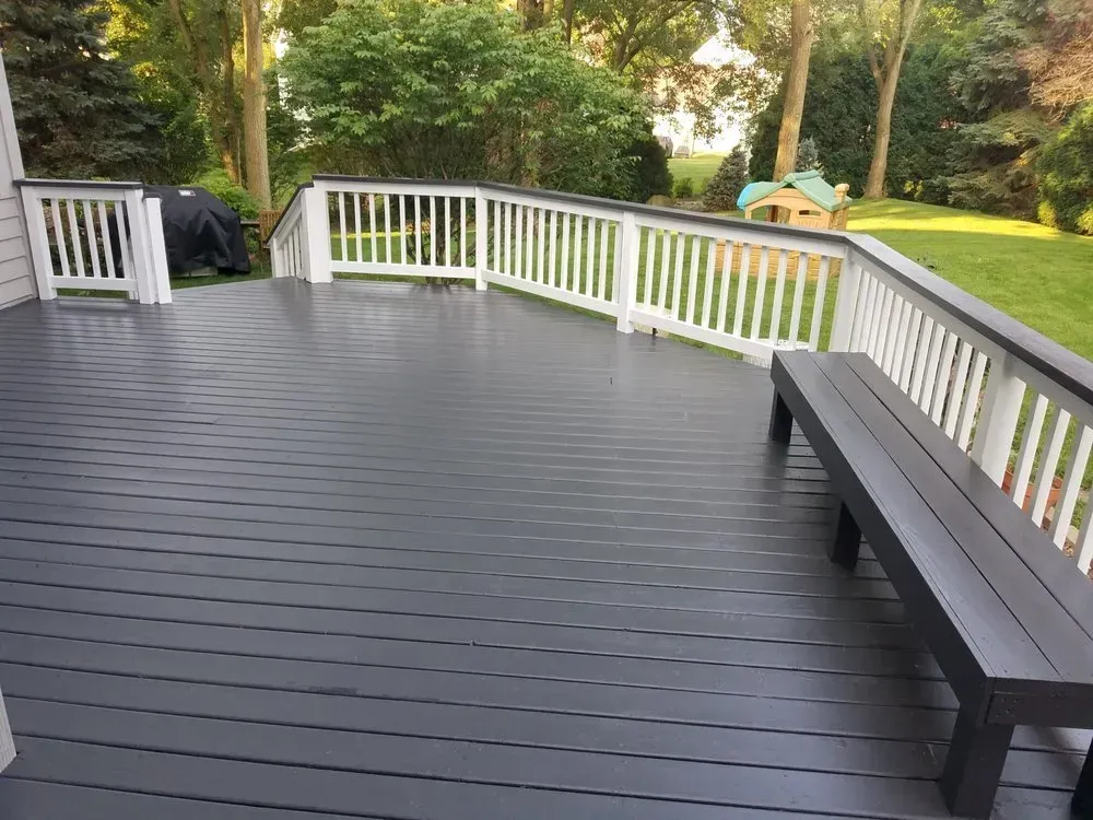 A gray deck with a white railing and a bench