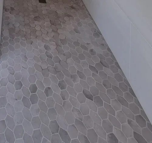 A bathroom floor with hexagonal tiles and a shower drain.
