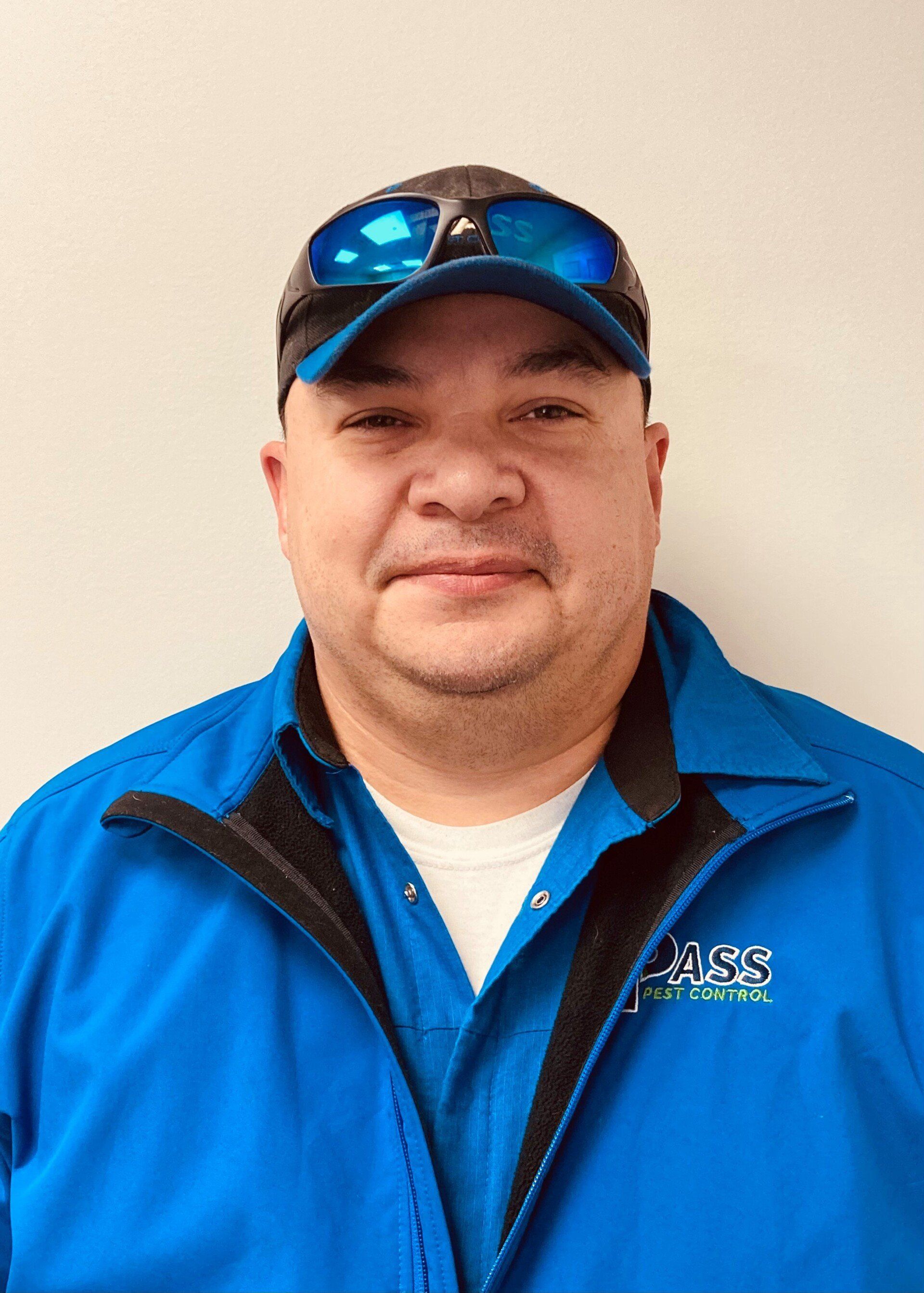 Man in blue jacket and cap with sunglasses on top, smiling at camera.
