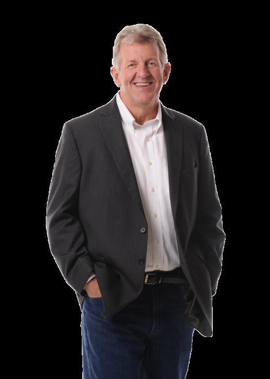 Man in a suit jacket, hands in pockets, smiling.