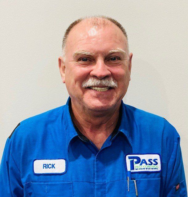 Rick, a man in a blue work uniform, smiles at the camera. He wears a name tag and has a mustache.