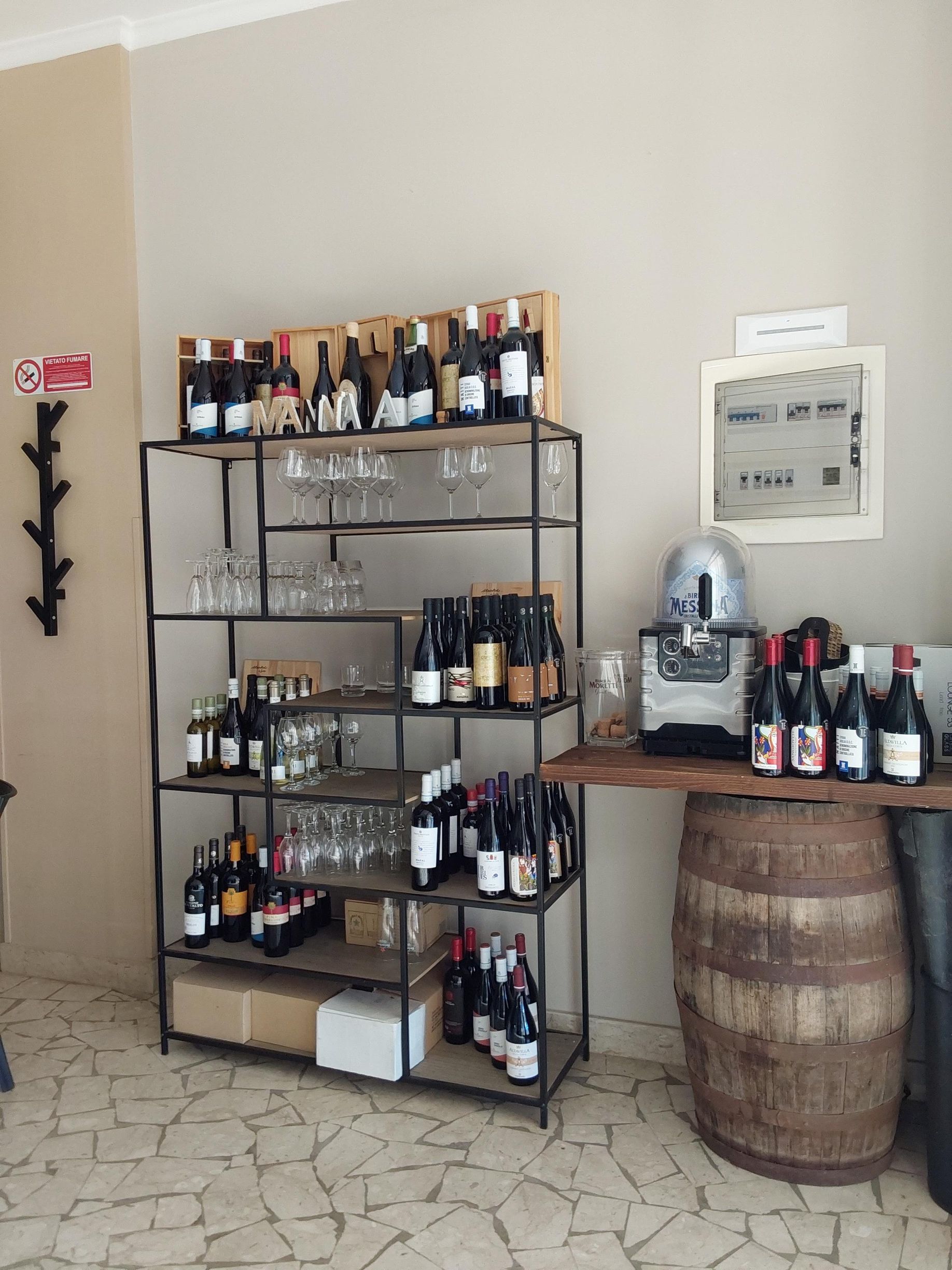 Bottiglie di vino esposte su scaffali di metallo e un tavolo ricavato da una botte in un angolo del negozio.