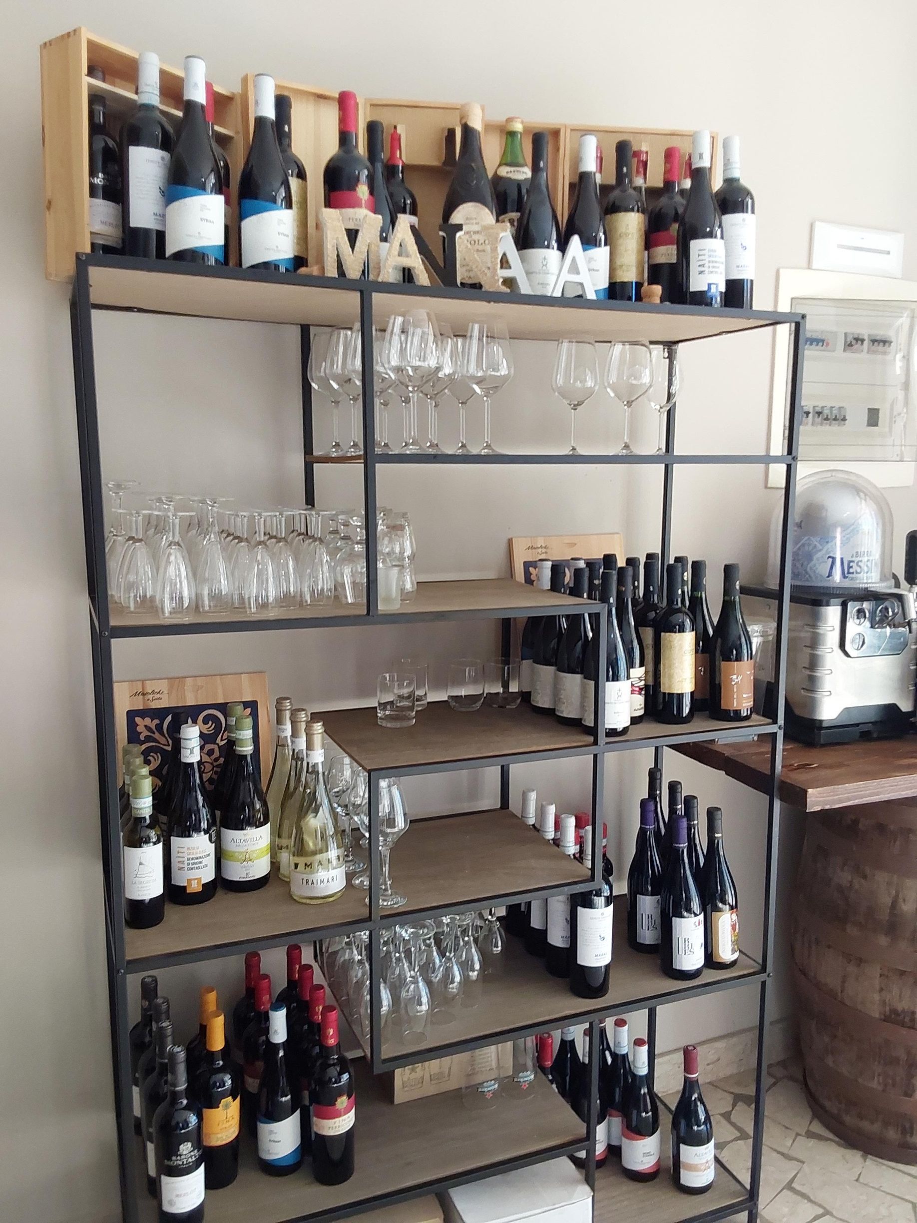 Bottiglie e bicchieri da vino disposti su una scaffalatura metallica in un bar o in una cantina domestica.