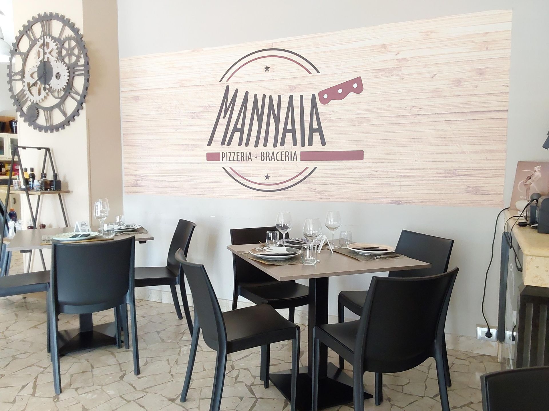 Sala da pranzo vuota del ristorante con sedie nere, tavoli apparecchiati e un grande logo a parete con la scritta