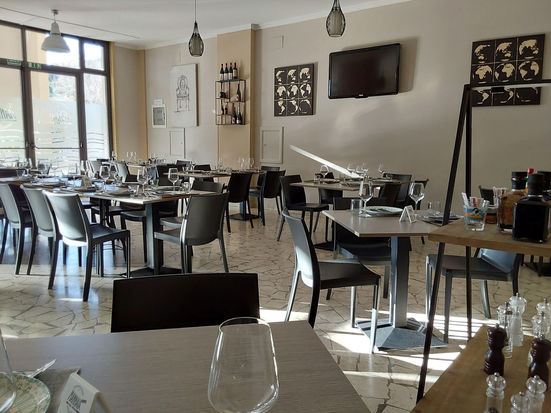 Interno luminoso e moderno di una caffetteria con tavoli e sedie vuoti, ampie finestre e opere d'arte alle pareti.