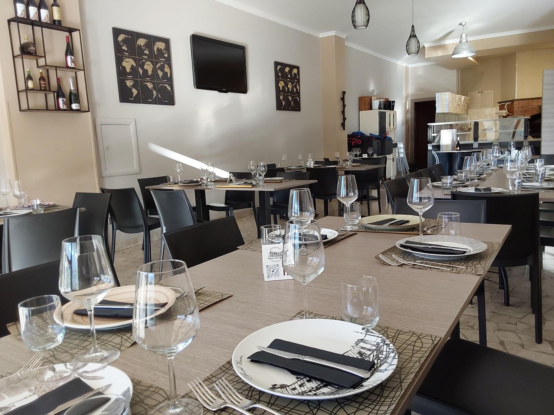 Sala da pranzo vuota del ristorante con tavoli apparecchiati, bicchieri da vino, sedie nere e opere d'arte alle pareti.