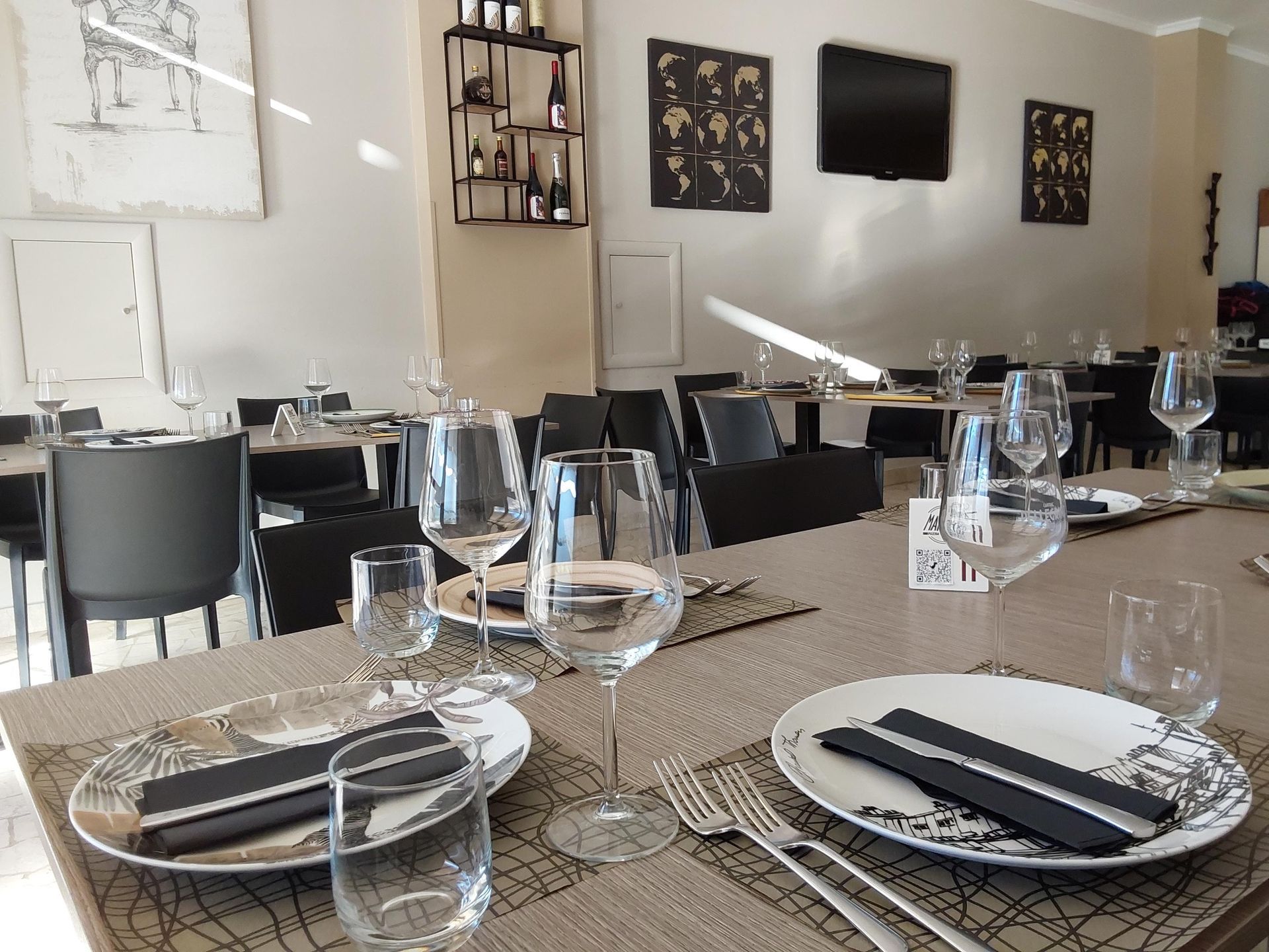 Elegante sala da pranzo di un ristorante con tavoli apparecchiati, bicchieri, sedie nere e opere d'arte alle pareti.