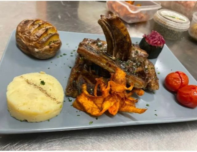 Carne grigliata servita su un vassoio grigio con purè di patate, verdure arrosto e pomodori a fette.