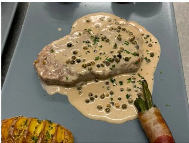 Bistecca in salsa cremosa al pepe con contorno di verdure grigliate, servita su un piatto blu.