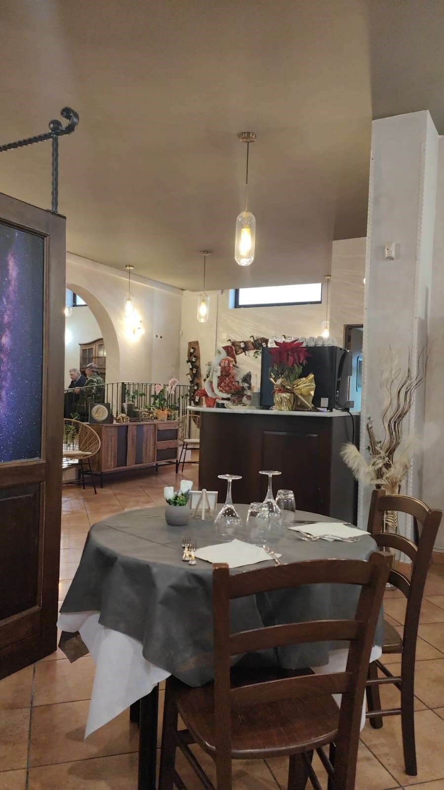 Accogliente zona pranzo con tavolo rotondo, sedie in legno, credenza, lampade a sospensione e TV a sinistra.