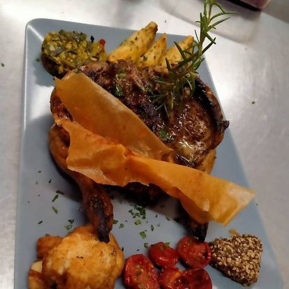 Carne arrosto servita con patatine fritte, verdure e contorni su un piatto quadrato blu.