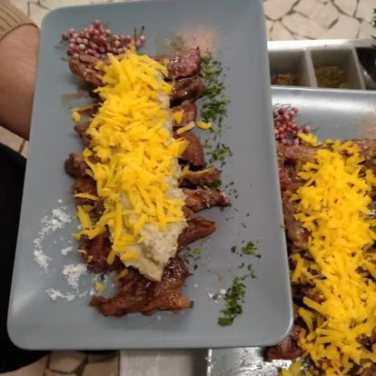 Carne grigliata ricoperta di formaggio giallo grattugiato e salsa su un piatto grigio, con riso e contorni a parte.