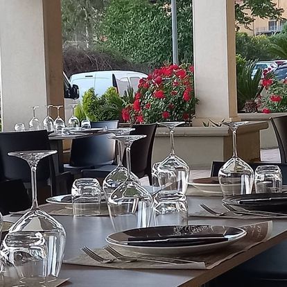 Elegante patio del ristorante con tavoli apparecchiati, calici da vino appesi e fiori rossi vicino alla finestra.