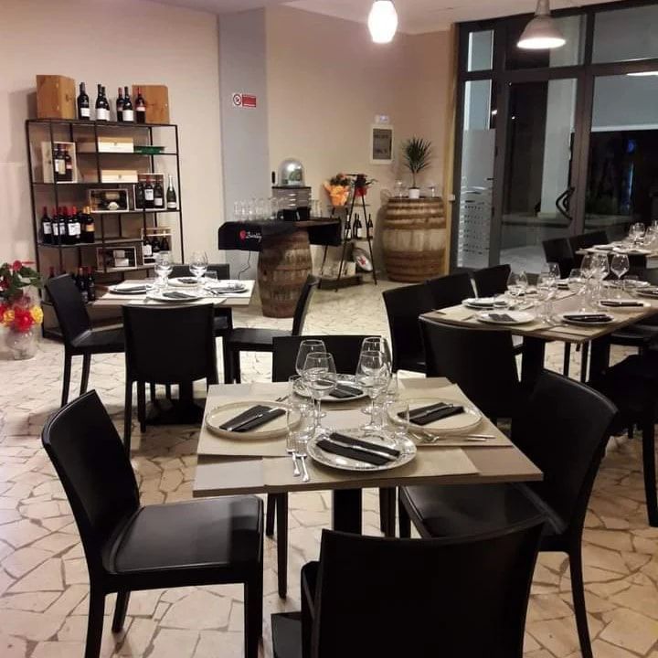 Elegante sala da pranzo del ristorante con sedie nere, tavoli apparecchiati, scaffali per il vino e botti vicino alla parete di fondo.