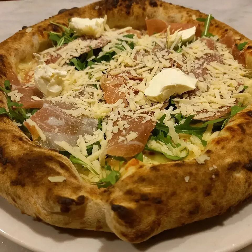 Primo piano di un piatto bianco con una pizza dorata condita con formaggio grattugiato e verdure.