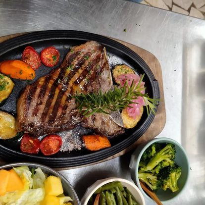Bistecca alla griglia su un piatto nero con verdure arrosto e contorni di broccoli e macedonia di frutta.
