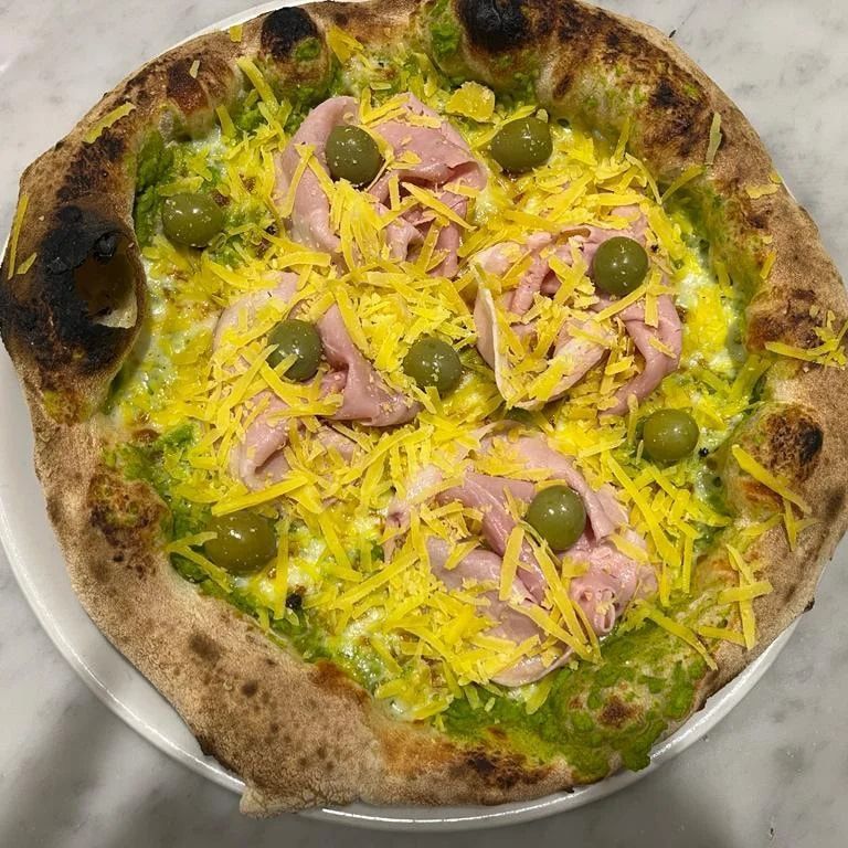 Pizza con olive verdi, formaggio grattugiato, prosciutto e salsa verde su un piatto