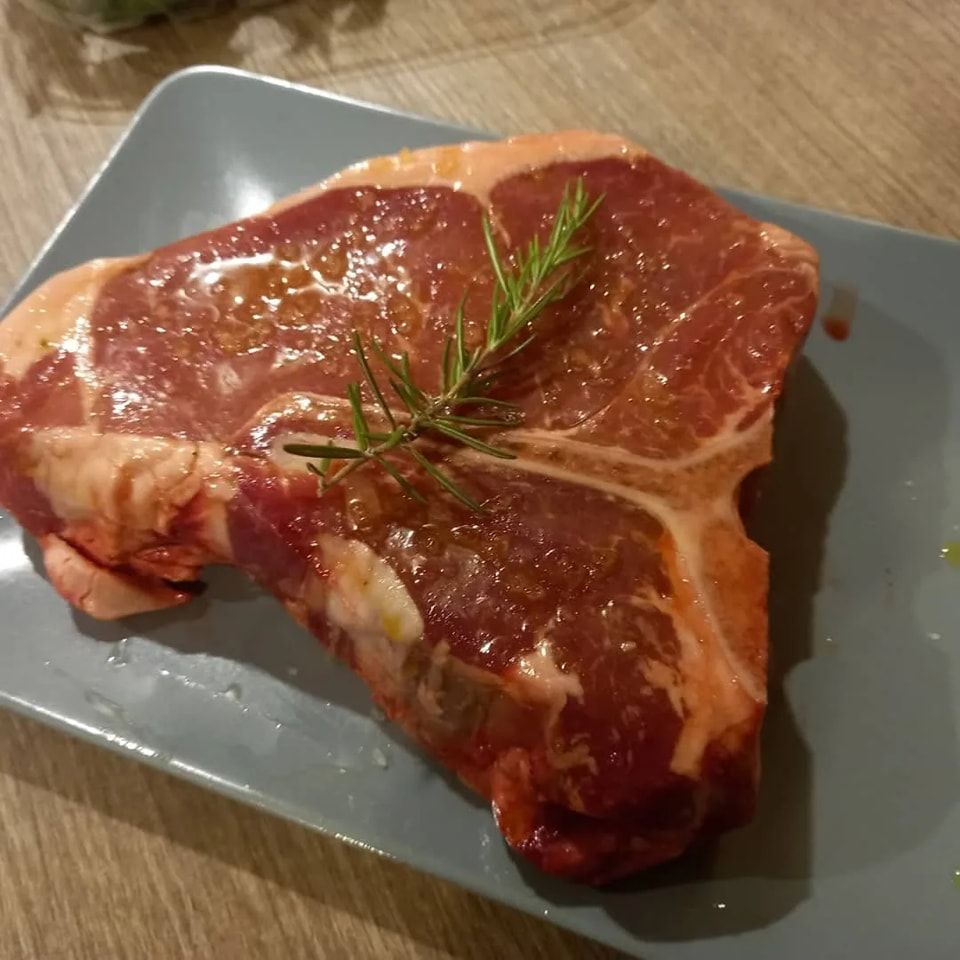 Bistecca cruda marmorizzata su un piatto grigio, guarnita con un rametto di rosmarino.